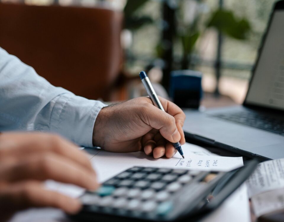 Free A person calculating finances with a calculator and pen on a desk indoors. Stock Photo