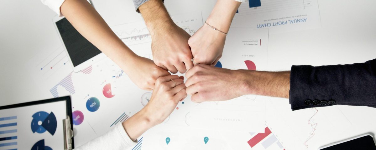 Free Colleagues celebrate success with a fist bump over financial charts depicting teamwork and unity. Stock Photo