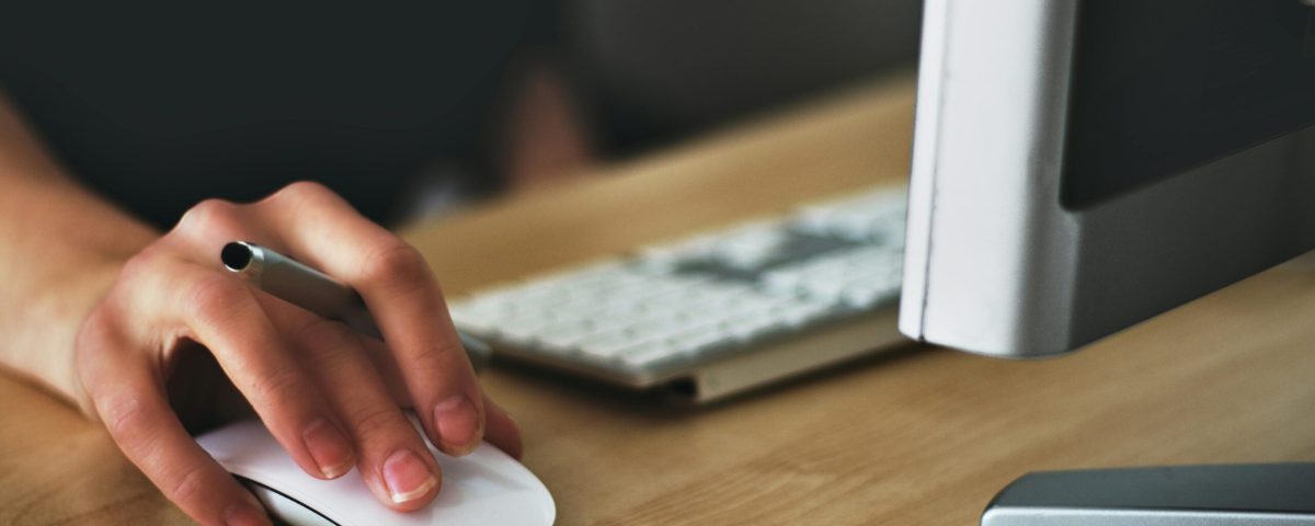 Free A hand using a wireless mouse at a modern desk setup with a computer and keyboard. Stock Photo