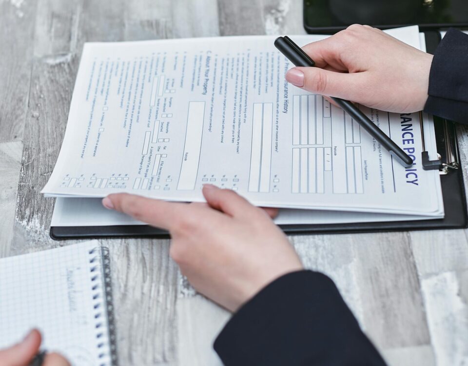 Free Close-up of hands analyzing insurance policy paperwork with pen on table. Stock Photo